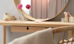 Eleganckie krzesło do toaletki z rattanowym oparciem, obok drewnianego blatu z kosmetykami i kwiatami.