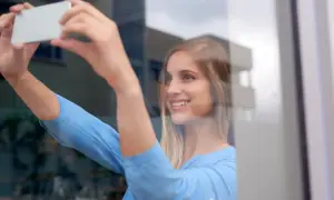 Uśmiechnięta blondynka robi sobie zdjęcie w lustrze, trzymając telefon.