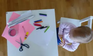 Dziecko przygotowuje materiały do zrobienia lustra z folii aluminiowej: kredki, nożyczki, taśmę, papier i folię.