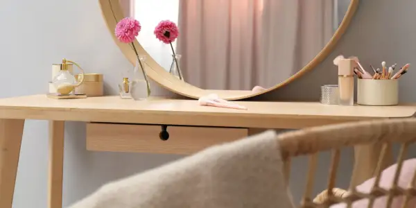 Eleganckie krzesło do toaletki z rattanowym oparciem, obok drewnianego blatu z kosmetykami i kwiatami.