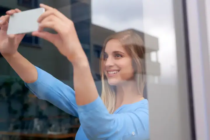 Uśmiechnięta blondynka robi sobie zdjęcie w lustrze, trzymając telefon.
